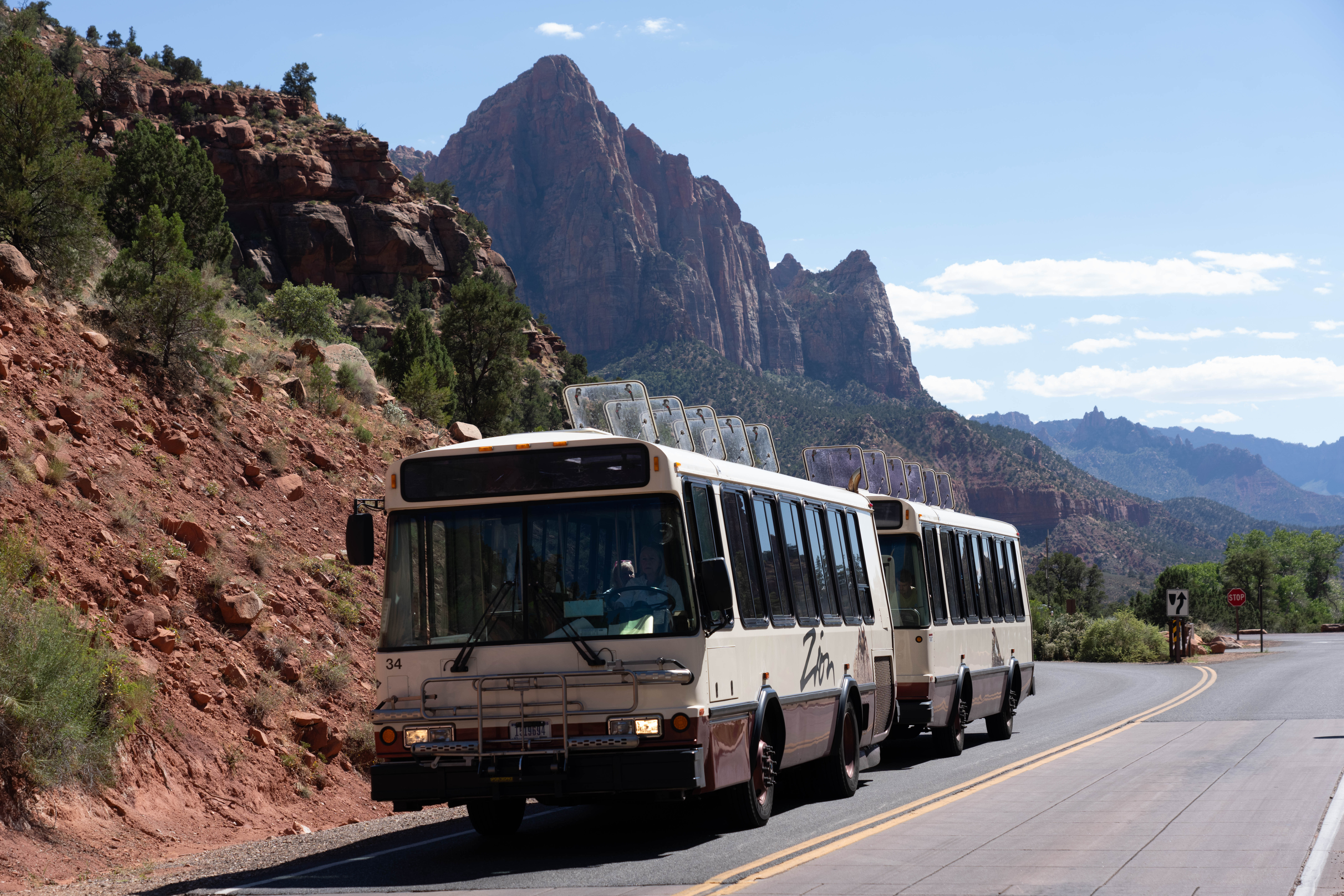 A Zion Canyon Line Shuttle driving with sandstone cliffs in the background.