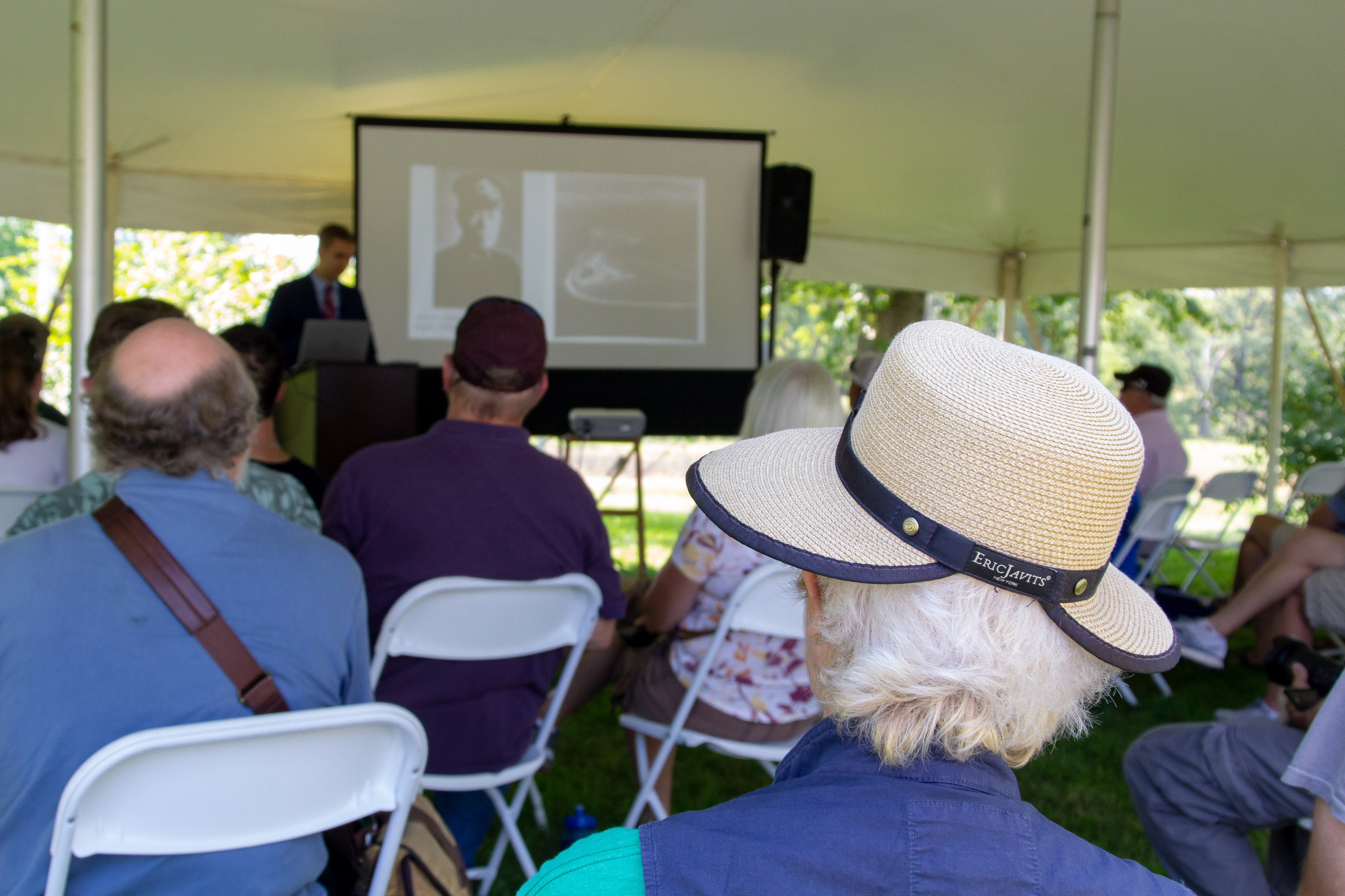A man giving a lecture at a podium under a tent.