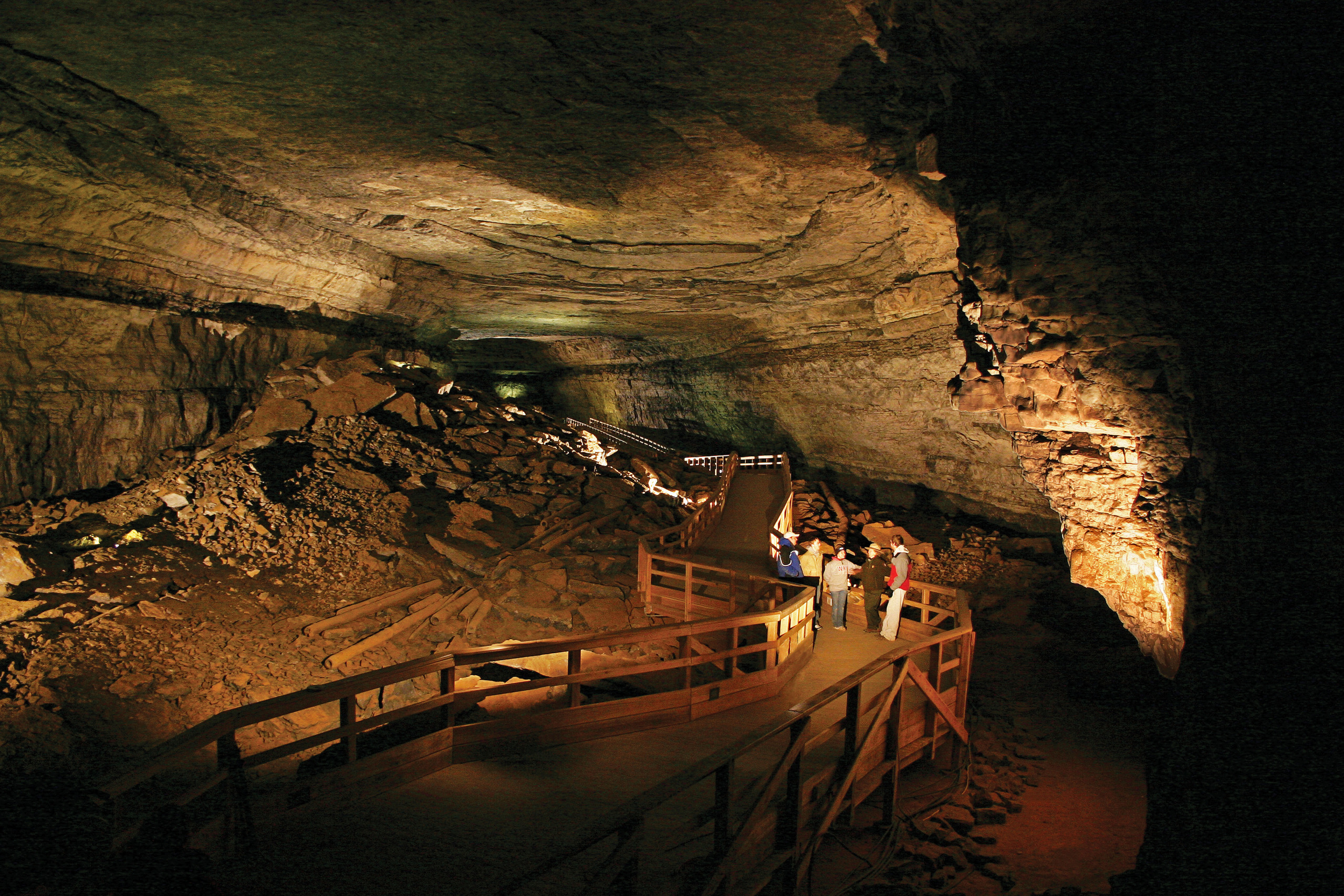 a large cave room lit up to show a boardwalk running through the middle of it with a group of people walking along it. 