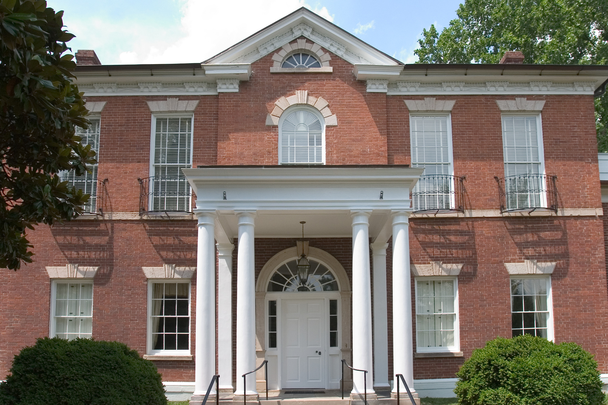 A two story brick building with white pillars adorning the front. There are white windows and white doors.