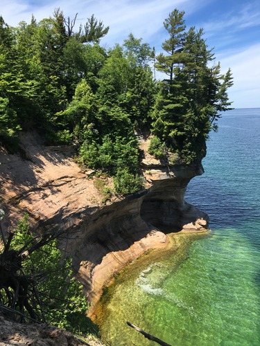 Standing on top of eroded rock cliffs and looking at more cliffs and the clear water of Lake Superior below
