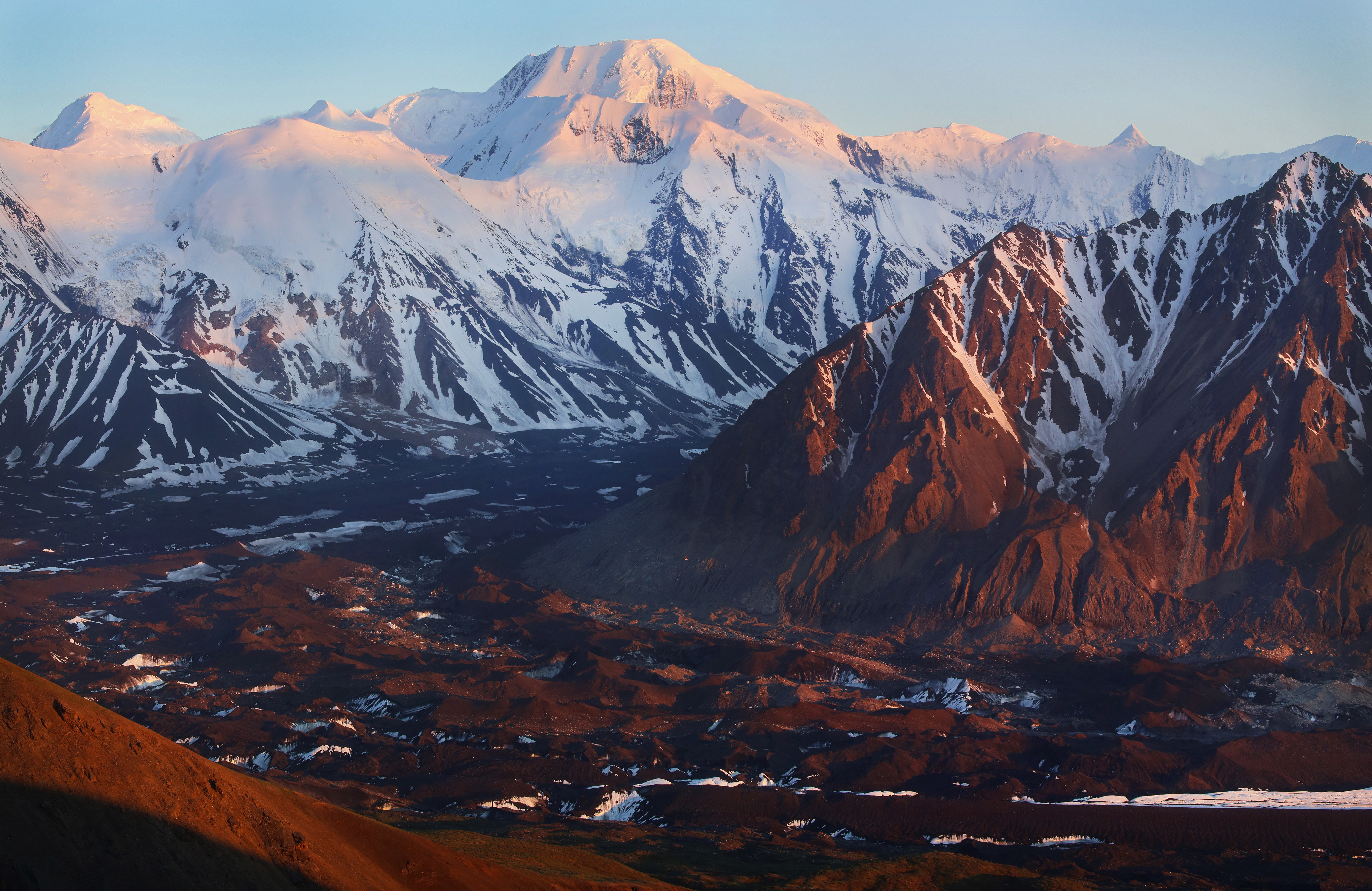 a rock-covered glacier flowing between snow-capped mountains