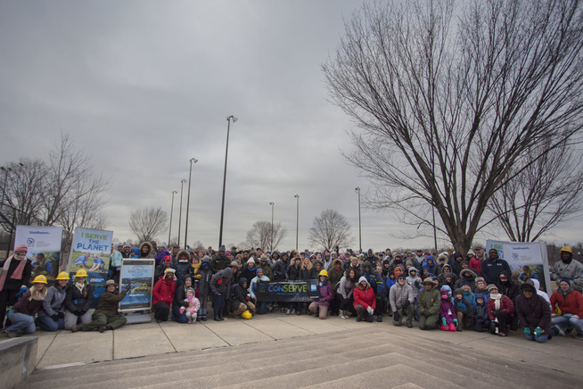 Around 100 people pose for a photo before they begin to pick up trash and remove invasive species in Anacostia Park.