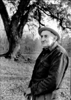 black and white photo of an old man wearing a hat, standing near a sprawling oak tree.