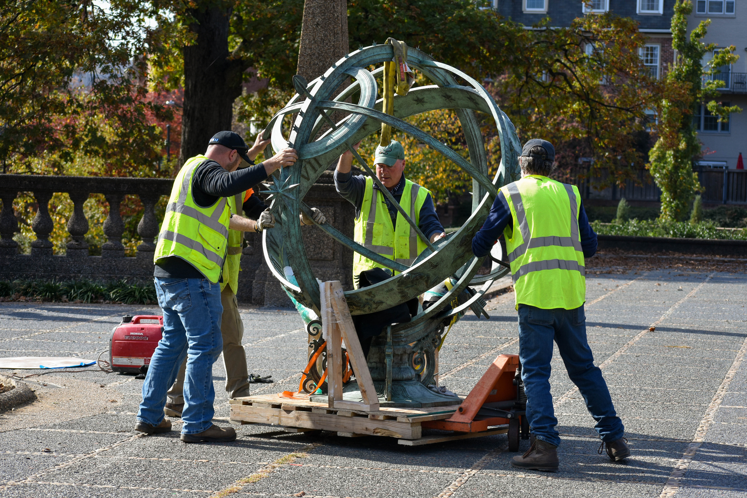 Four push a green-tinted armillary sphere that is secured to a wooden platform with yellow nylon straps.