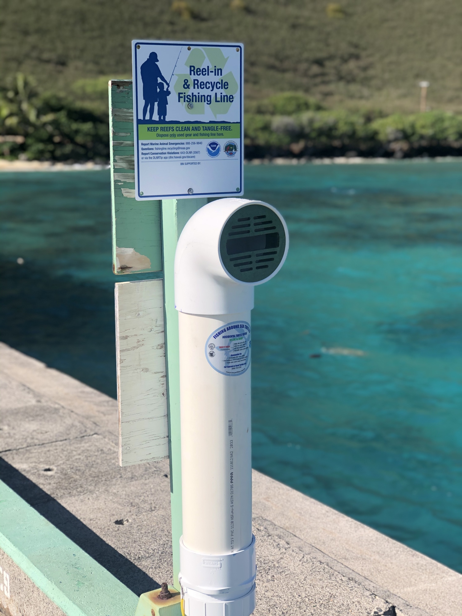 A fishing line receptacle on a dock with tropical blue water in the background.