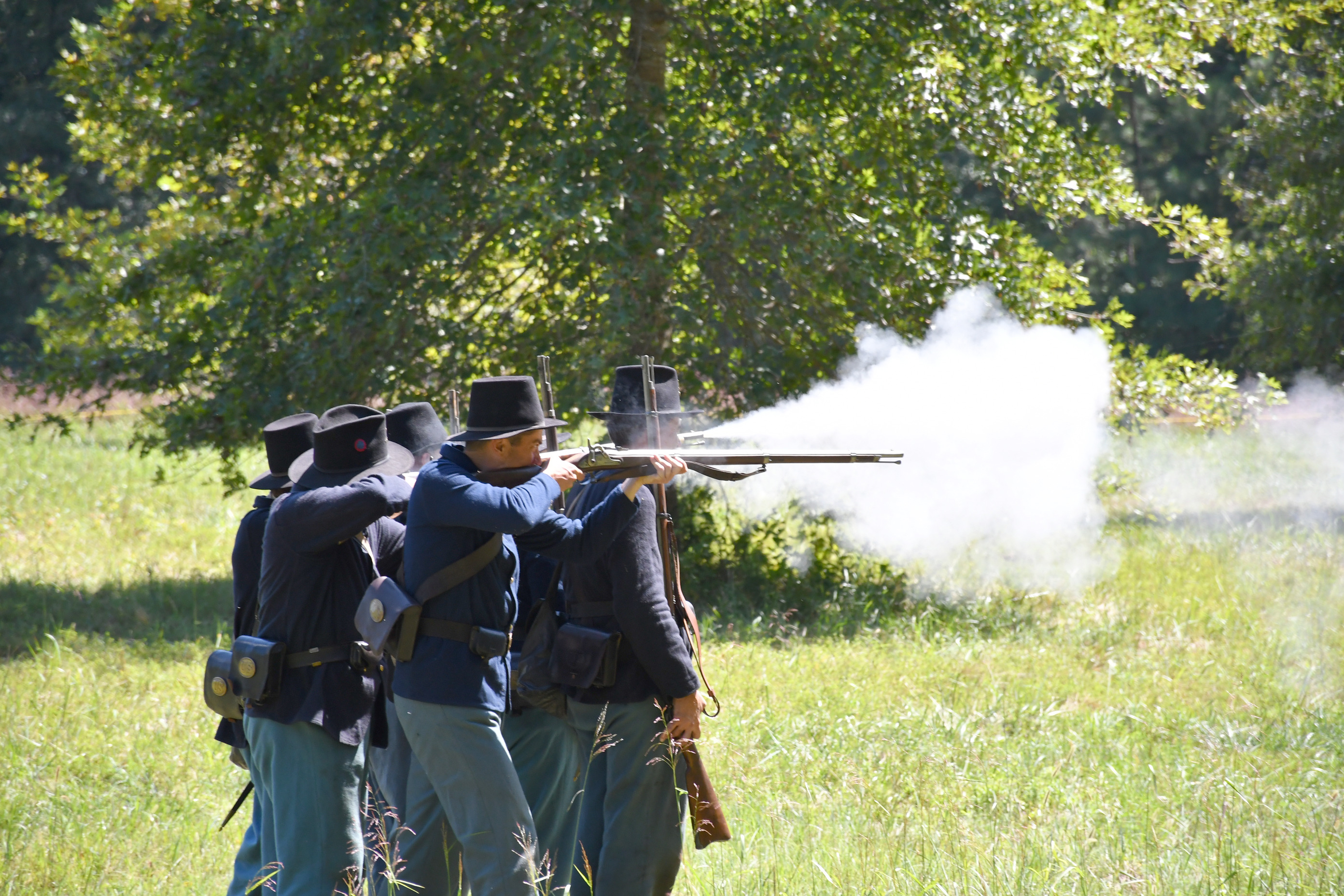 Six men in blue US Army uniforms fire rifles in close formation.
