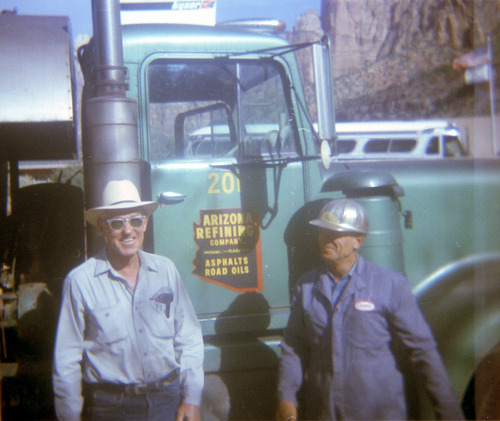 Workers smiling while standing next to a construction vehicle.