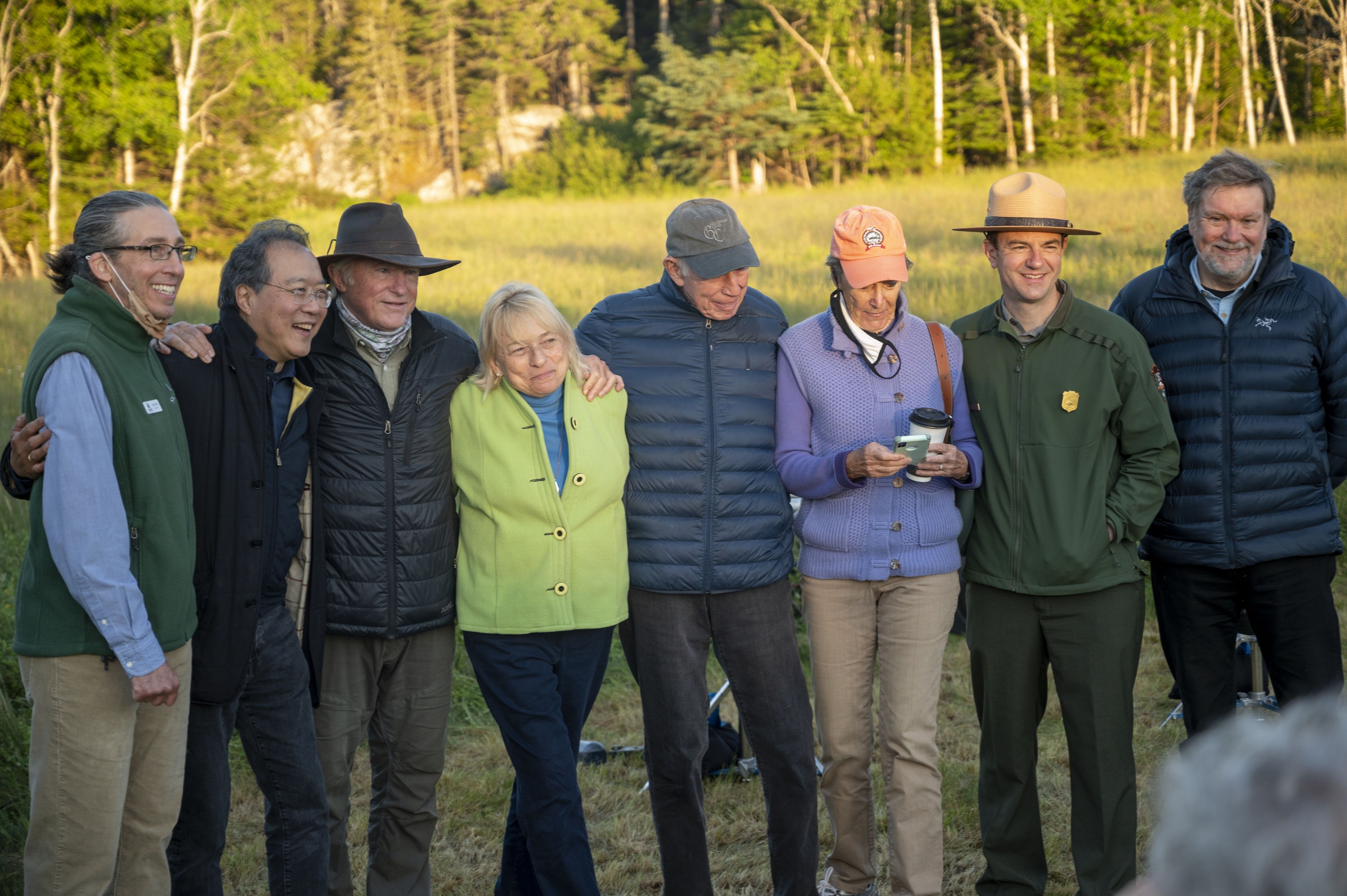 Eight people line up in preparation to have a photo taken at the edge of a field bathed in sunlight.