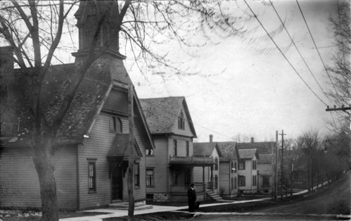 Historic black and white photo. The wooden Thompson AME Zion Church is on the far left. The view is looking past the front of the church, north up Parker Street.
