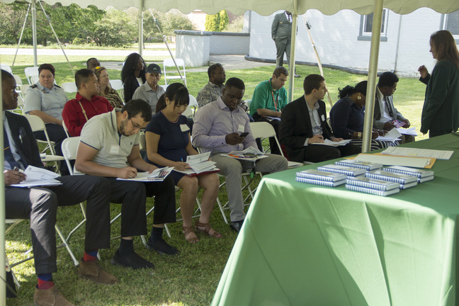 Several people sitting in chairs under a tent write on paper forms.