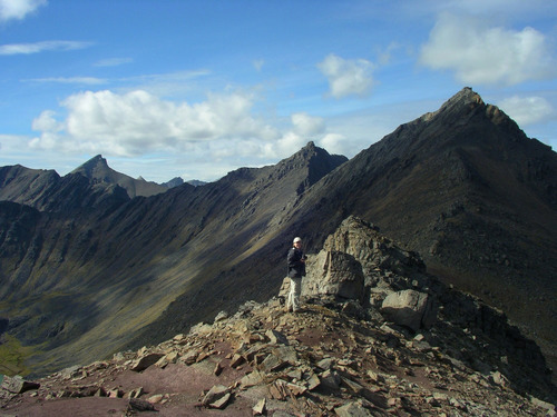 person standing on narrow mountain ridge with peaks extending into the distance
