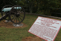 a white sign with red letters next to a cannon