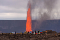 Large fountain of lava within Halemaʻumaʻu crater with visitors on the rim. 