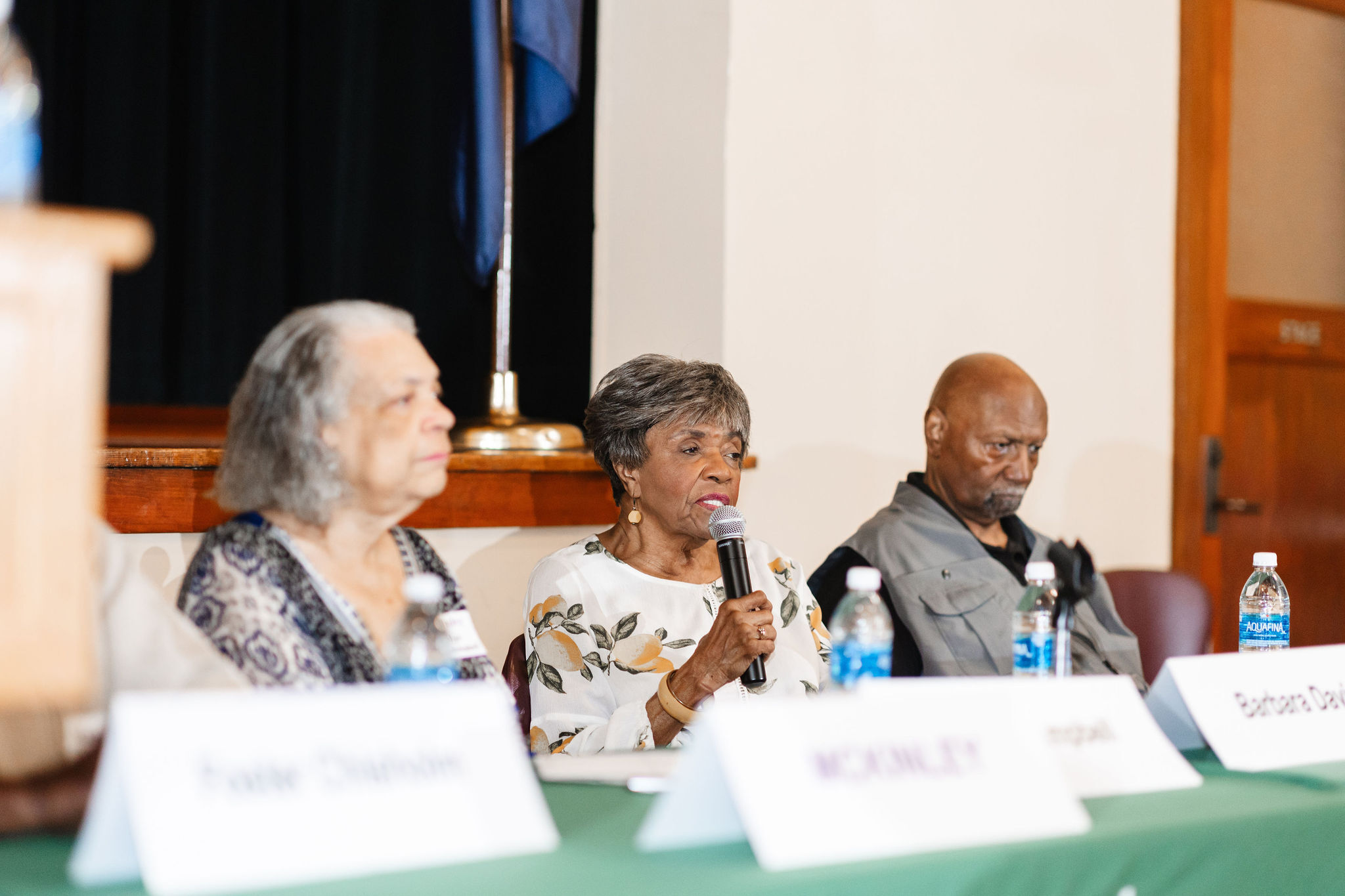 an older african american woman in a white shirt speaks into a microphone