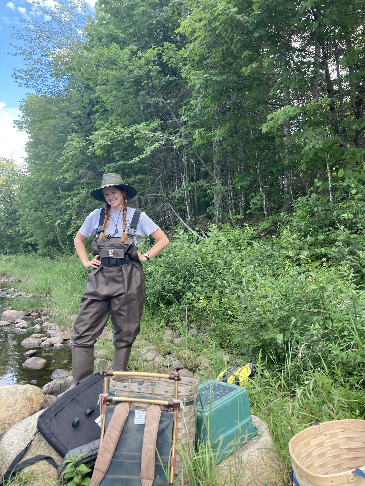 A researcher in waders stands behind a pile of equipment such as baskets and storage bins.