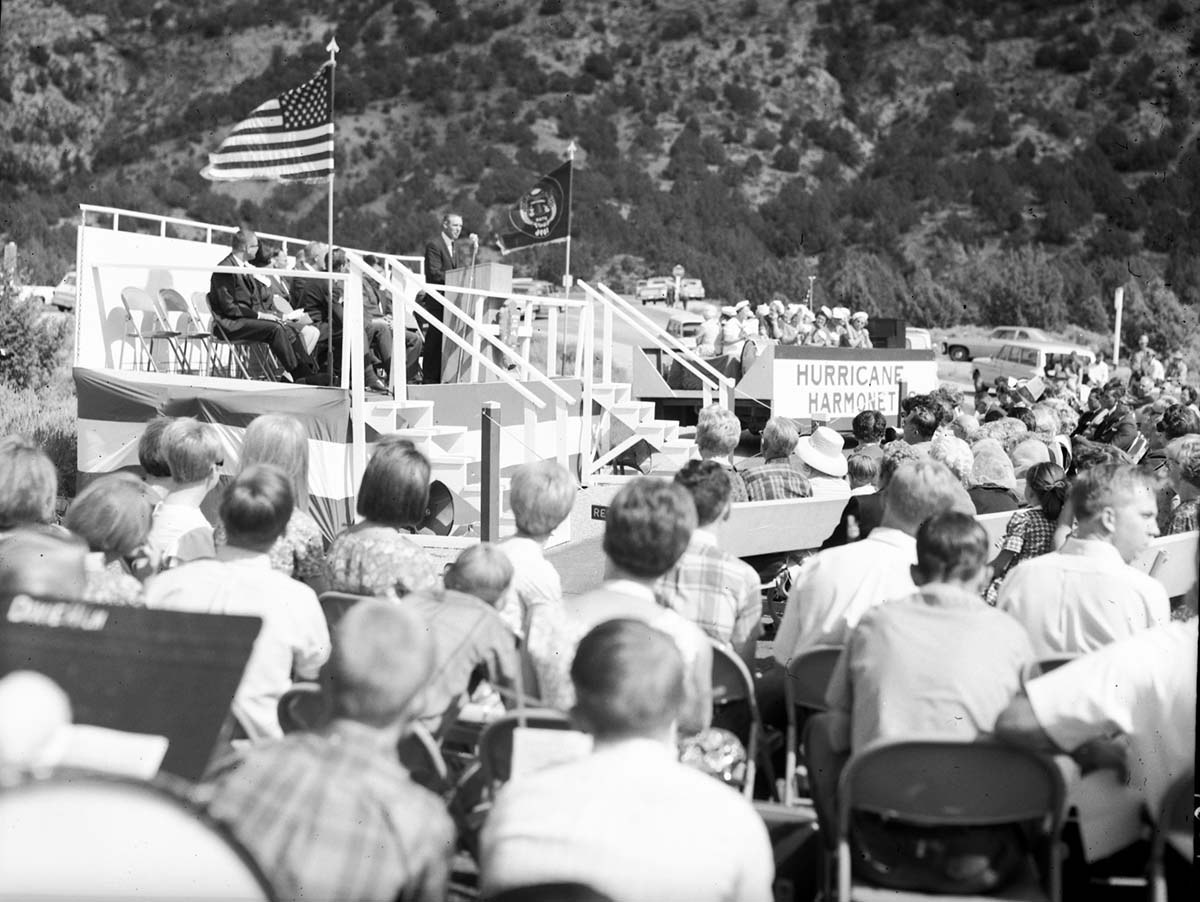 Warren F. Hamilton, Superintendent of Zion National Park, addressing visitors from podium at dedication of Taylor Creek road (Kolob Canyons). Note Hurricane Harmonetts [Harmonettes] singing group at right.