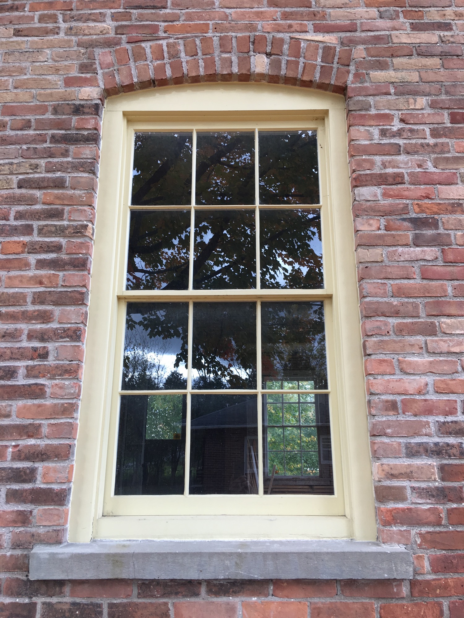 A window with cream trim surrounded by bricks with a brick arch above the top of the window. 