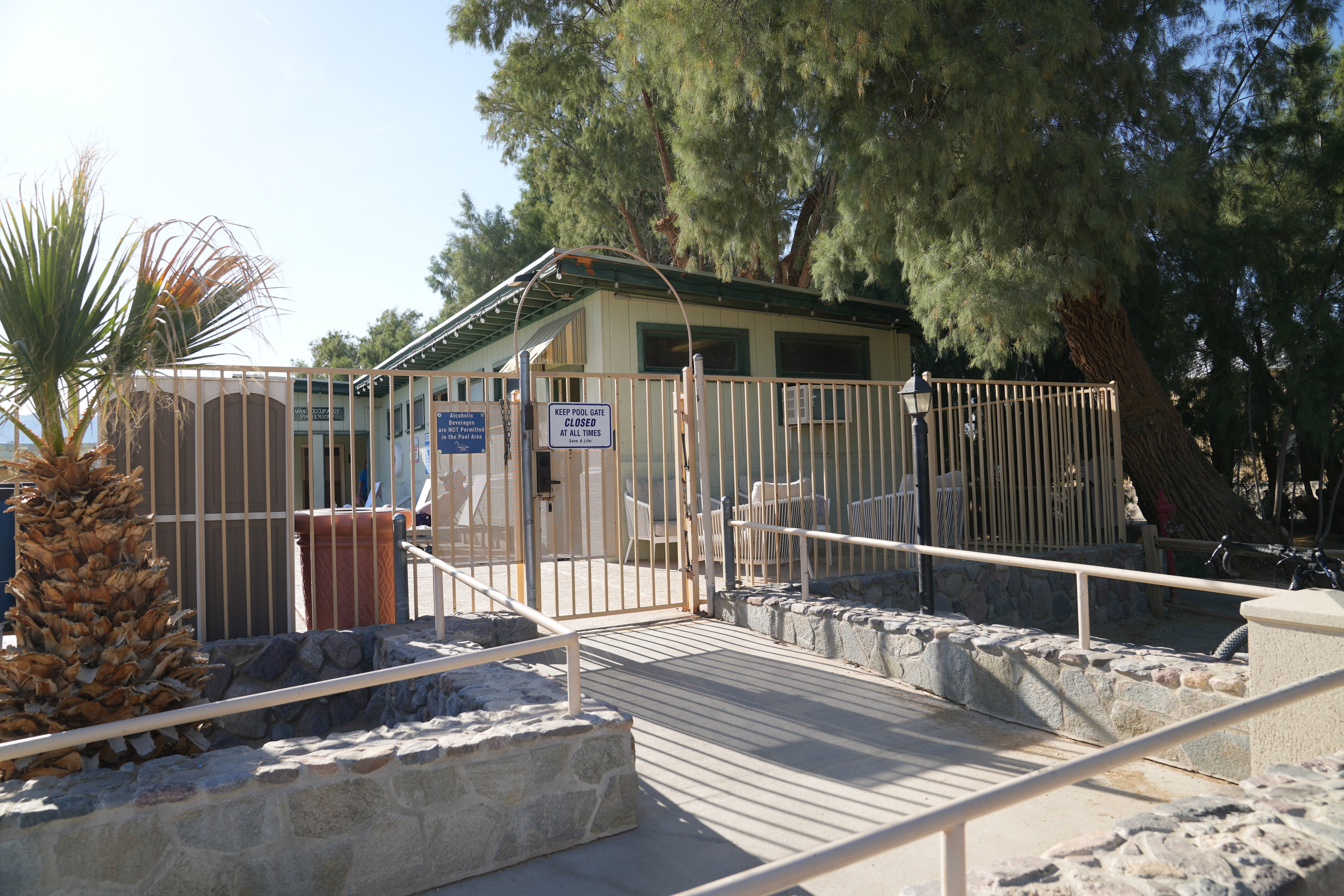 A ramp that leads up to The Ranch's pool.  The ramp has railing on both sides and is even and concrete. The gate is manual.