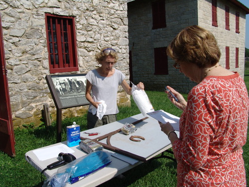 conservator and park staff looking at a table with an iron artifact and supplies laid out to carry out cleaning and coating services