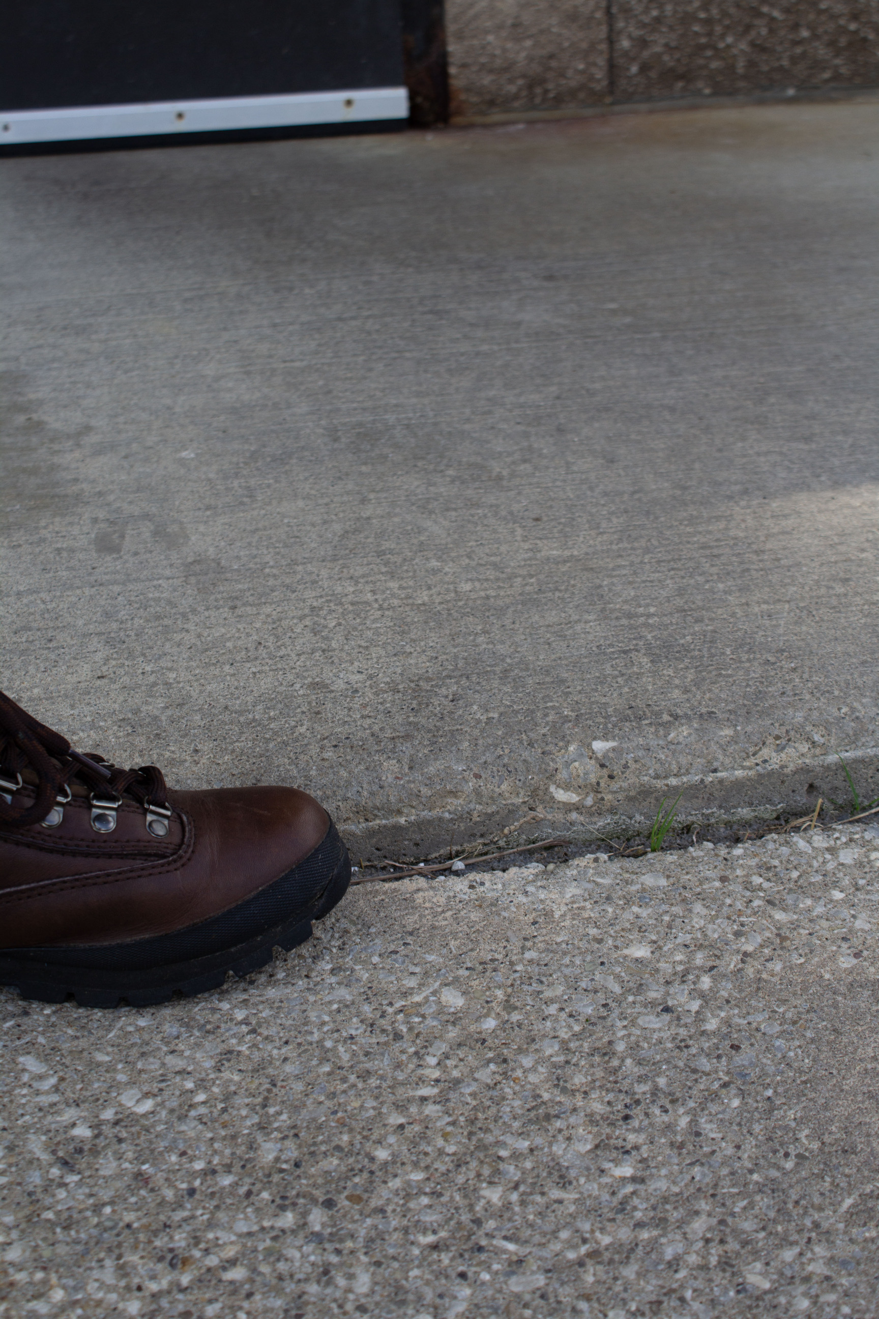 A brown boot positioned along a linear step up between two areas of concrete; the step is about as high as the black sole of the boot.