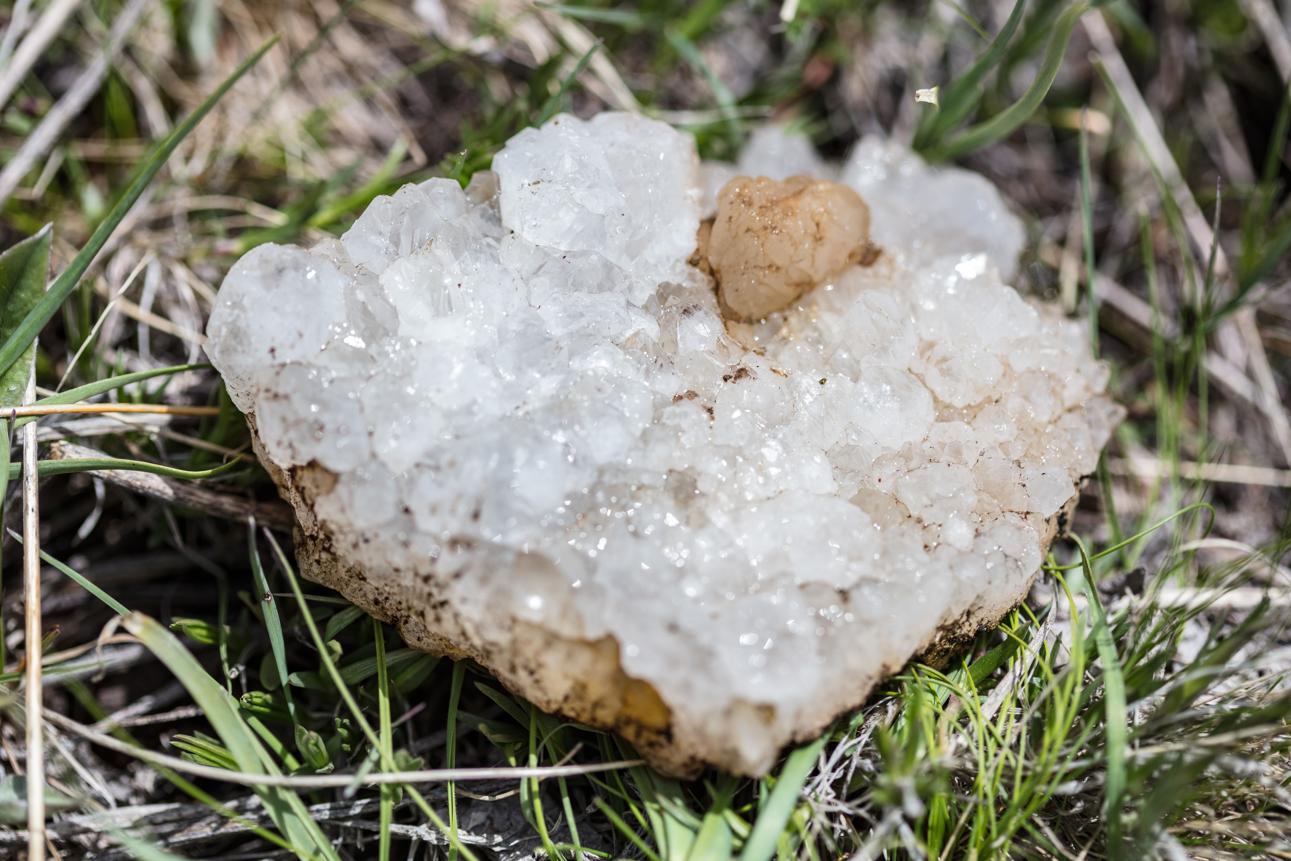 A rock of quartz crystals sitting in grass.