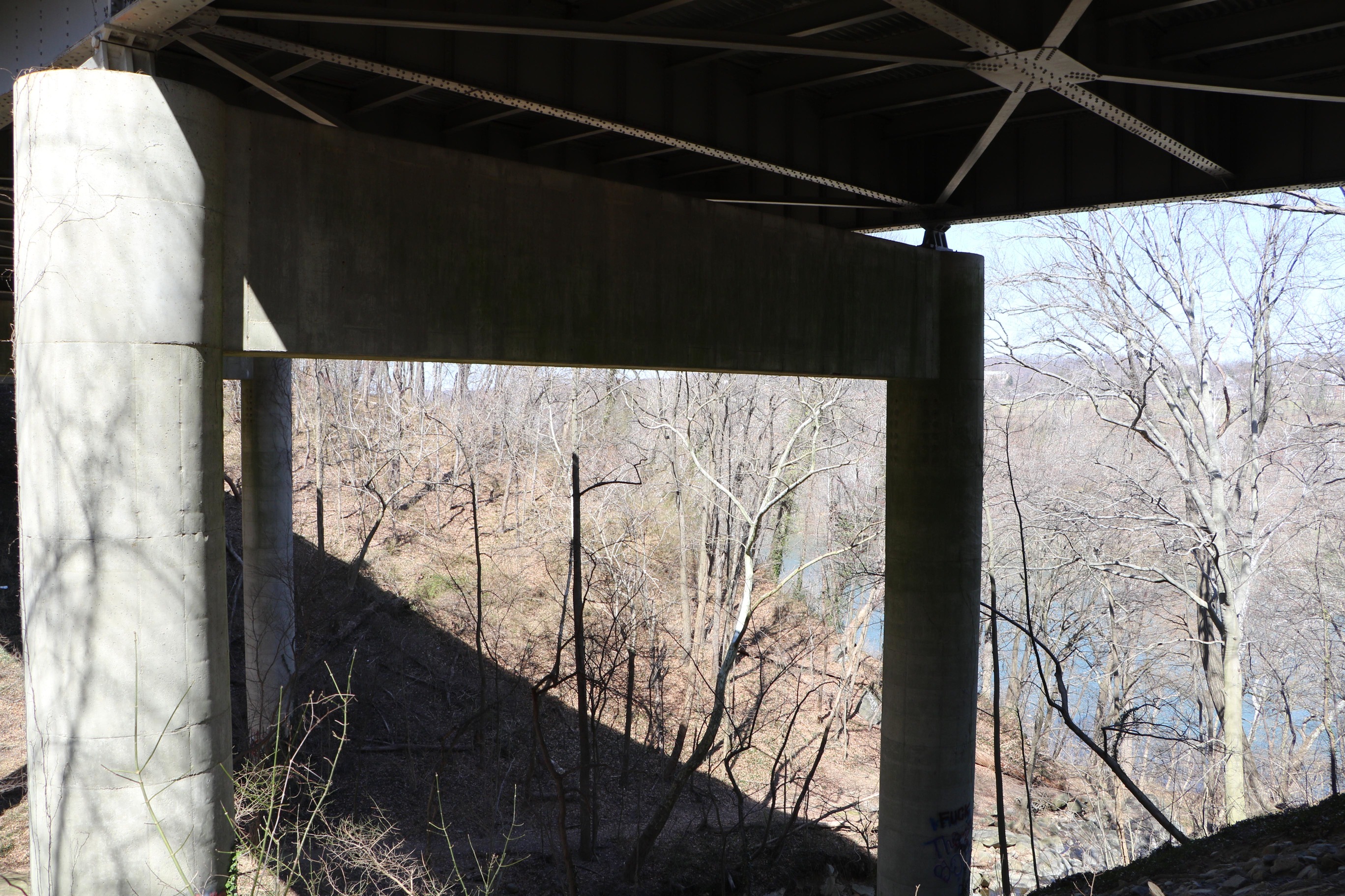 Image showing underside of bridge featuring steel beams, reinforced concrete columns and a view of the Potomac River in the distance.