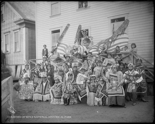 Large group in ceremonial regalia with Chilkat robes; dance sticks; masks rattles; etc.