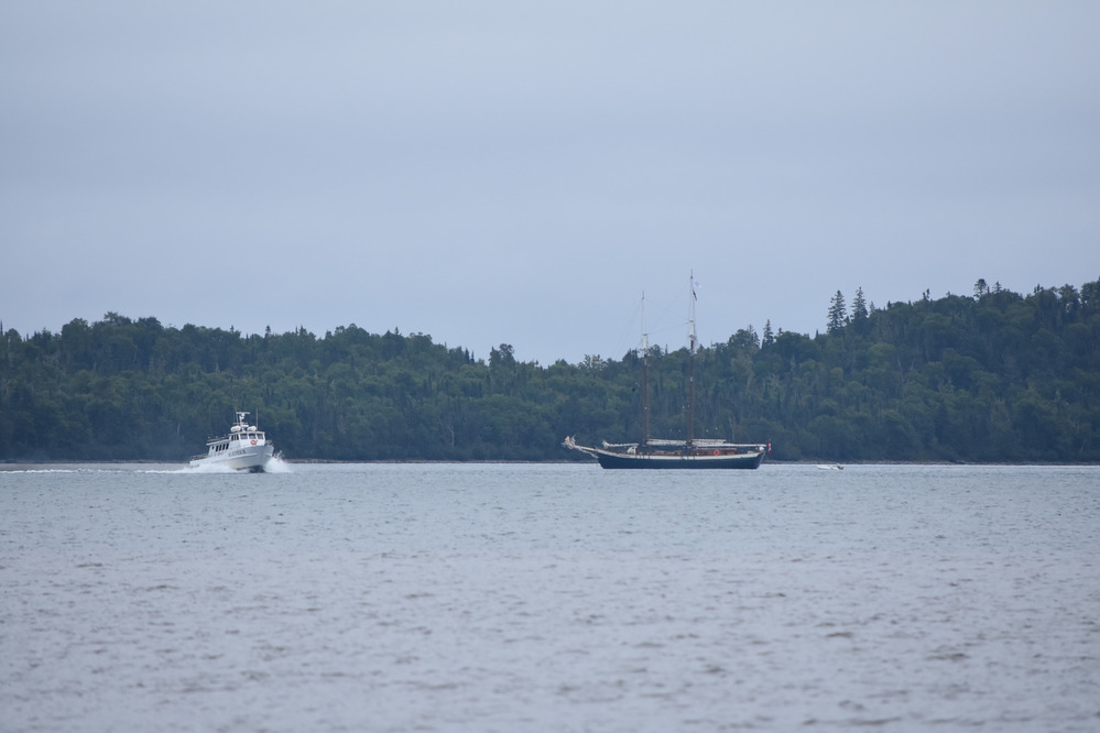 A white motorboat passes sailboat at anchor.