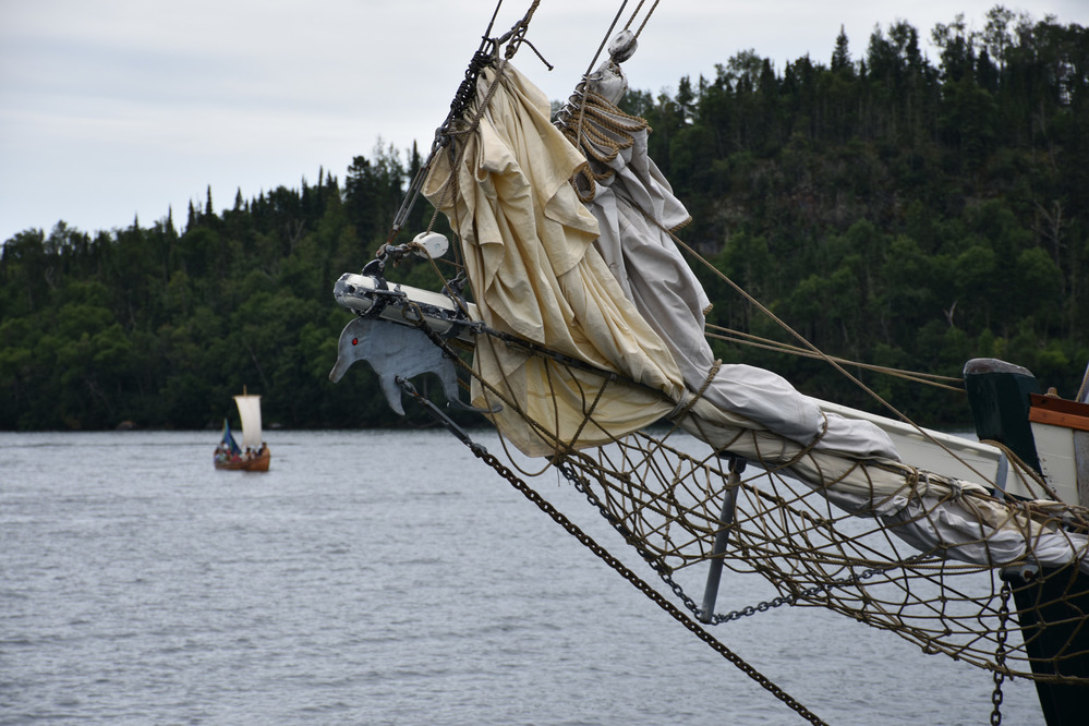 Detail of sailboat bowsprit, sailing canoe and forested island.