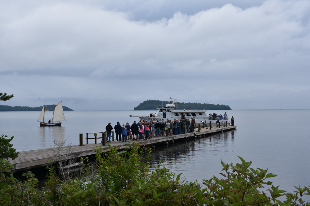 Dock with people in line, motor vessel, sailboat and island in distance