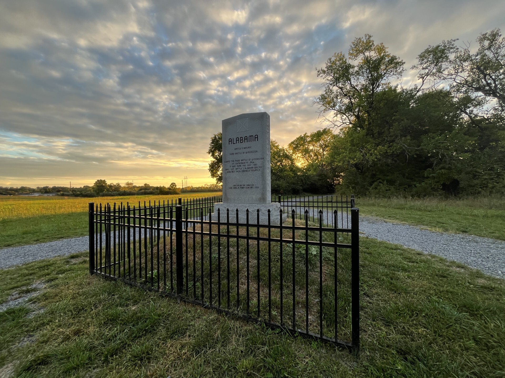 A stone monument surrounded by a black metal fence, underneath a vibrant sunset sky. 