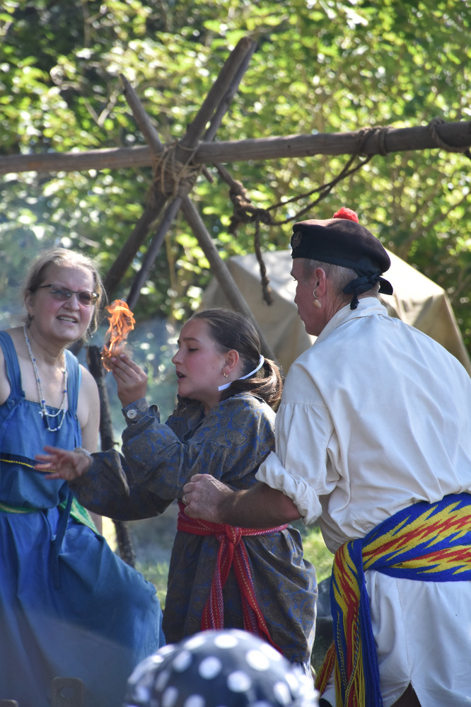 Reenactor holds burning tinder and two others closely watch.