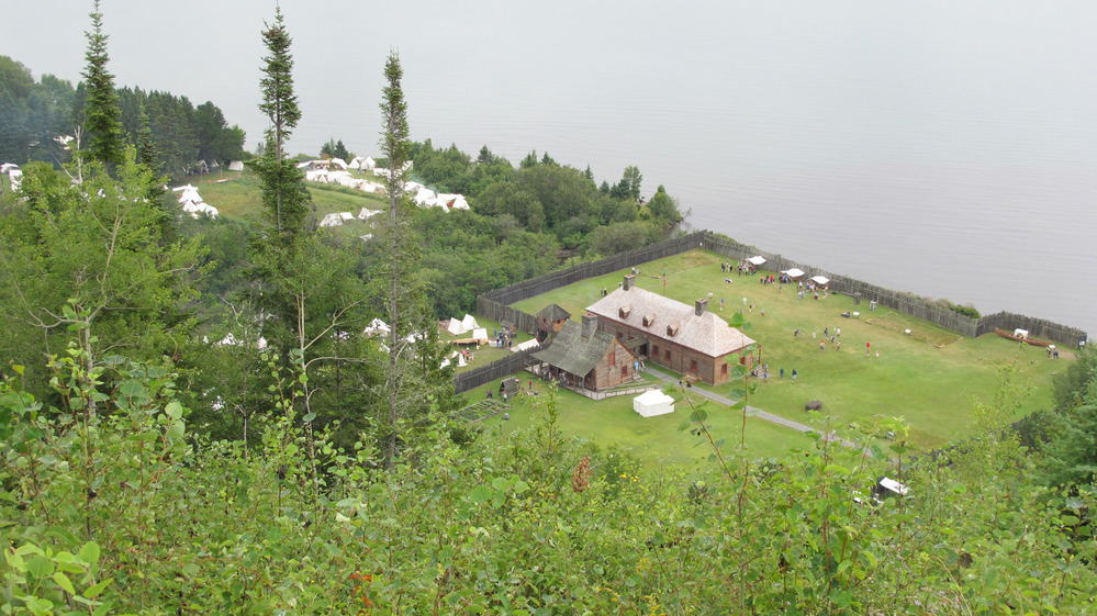 White canvas tents stand out over brown buildings and stockade fence.