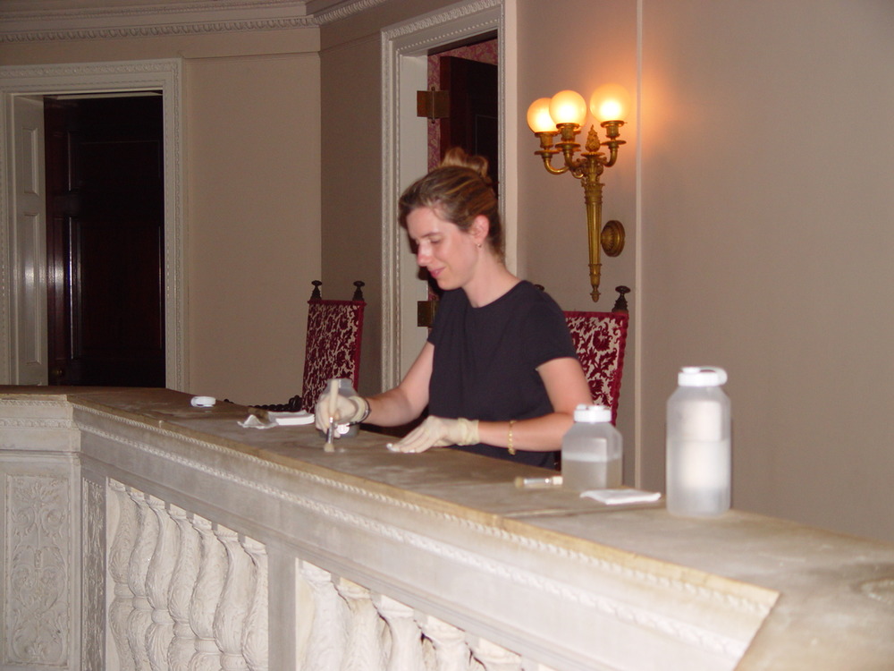 The marble balustrade rail has become heavily soiled with lipids from the hands of visitors touching the surface.  A conservator tests methods for gently cleaning the surface with soapy solutions and a soft brush.