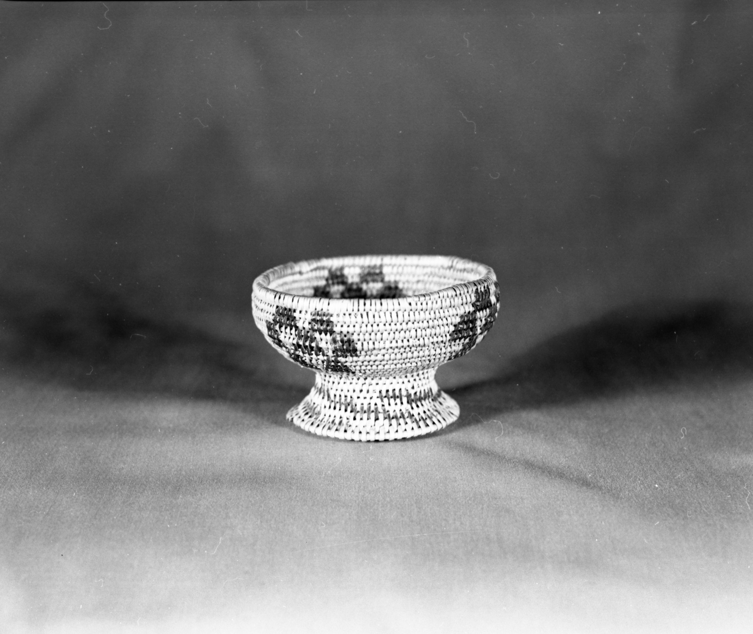 Private Collection. Object: Miwok basket. Dimensions: 4 1/2 x 2-3/4". Materials: Redbud & unidentified split shoot (possibly Ceanothus Intergermus). Technology: Pedestal of basket in single rod. Cup in three rod. In both cases, fag ends trimmed on work face, moving ends trimmed on interior. Collection HIstory: Made by Matilda, a Sonora Miwok. Photographed by Michael Dixon. Catalogued by Craig Bates and Barbara Beroza. Yosemite Collections, National Park Service.