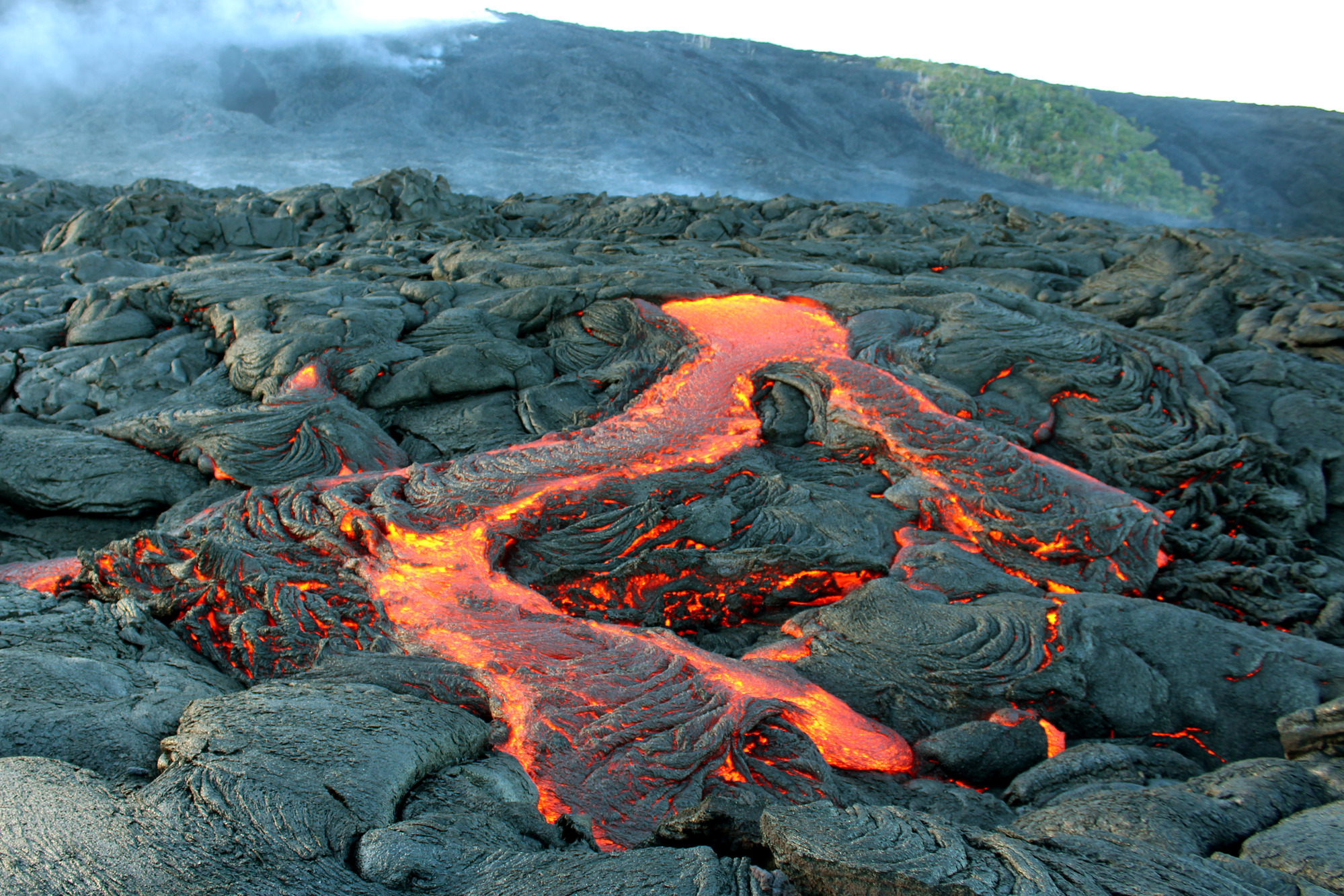 Molten lava flow with steaming hills behind