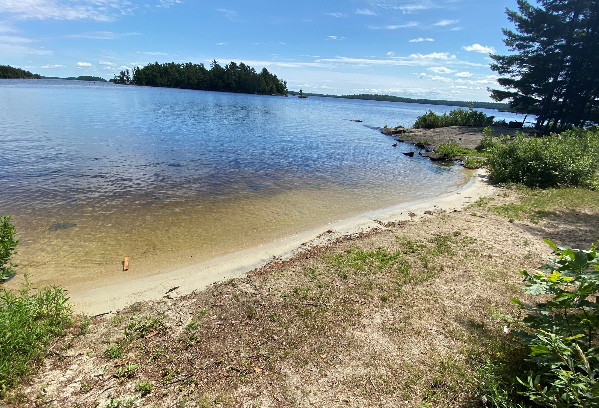 View of houseboat site beach access from shore with site core on right of image. An tree covered island is in the background across the water.