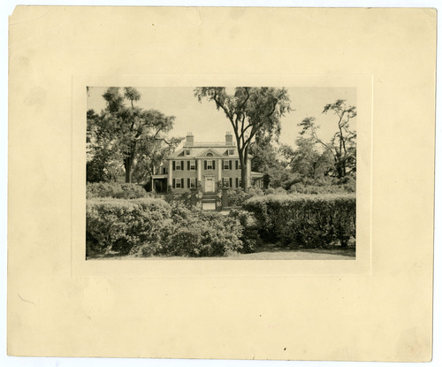 Photo of Georgian mansion with bushes in foreground.