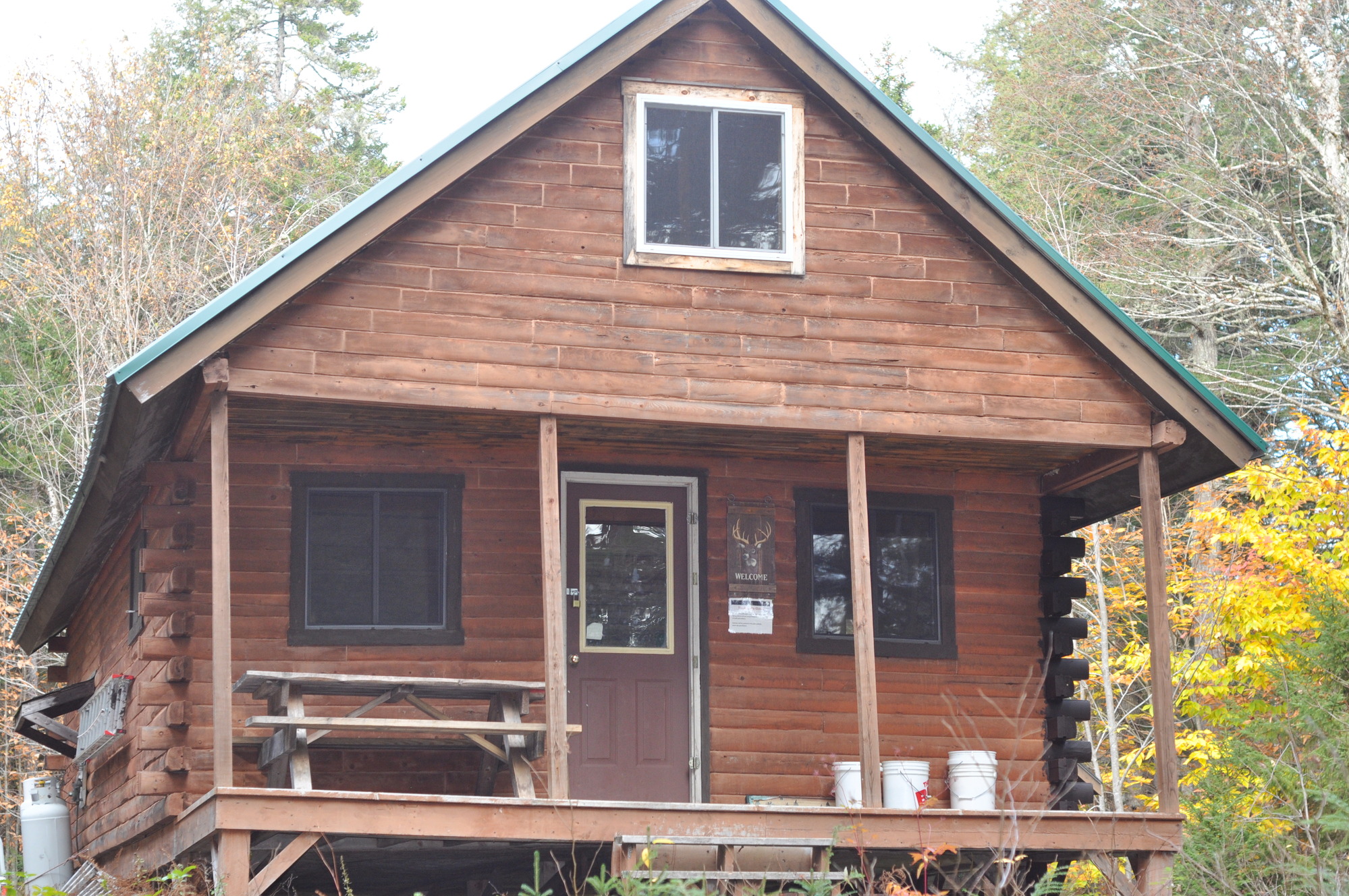 A log cabin from the outside with picnic table is on the porch.