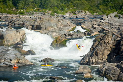 A kayaker going down a waterfall with two friends in kayaks waiting at the bottom. 