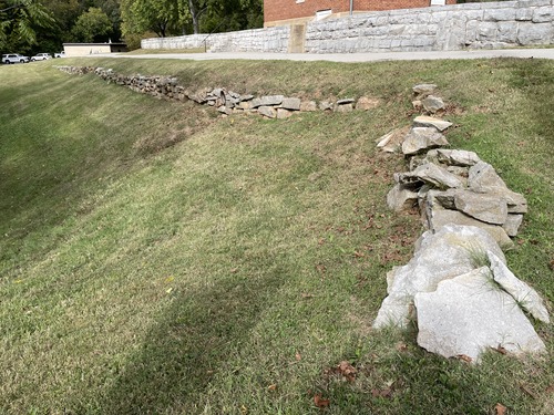 Deteriorated stone wall with grass growing in and around it.