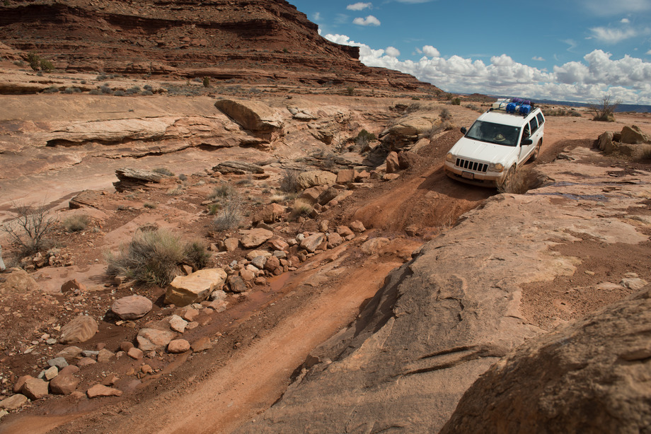 a white jeep drives down a steep, muddy slope.