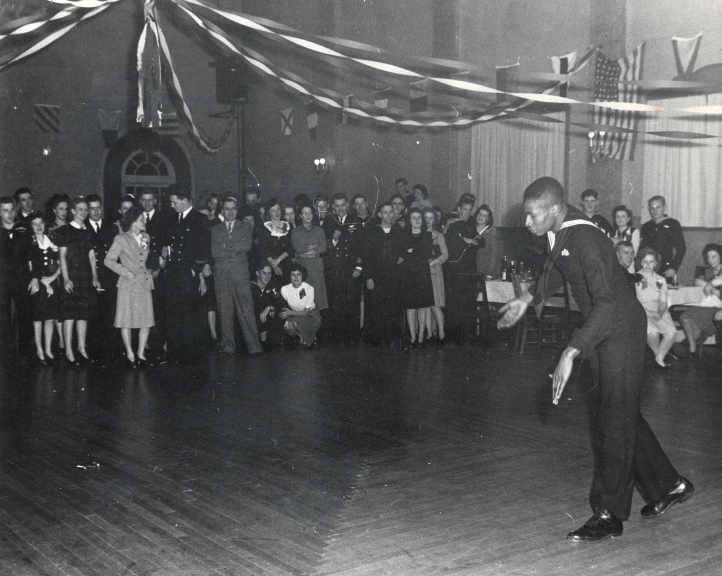 Black and white photo of African American sailor dancing solo as a crowd watches.