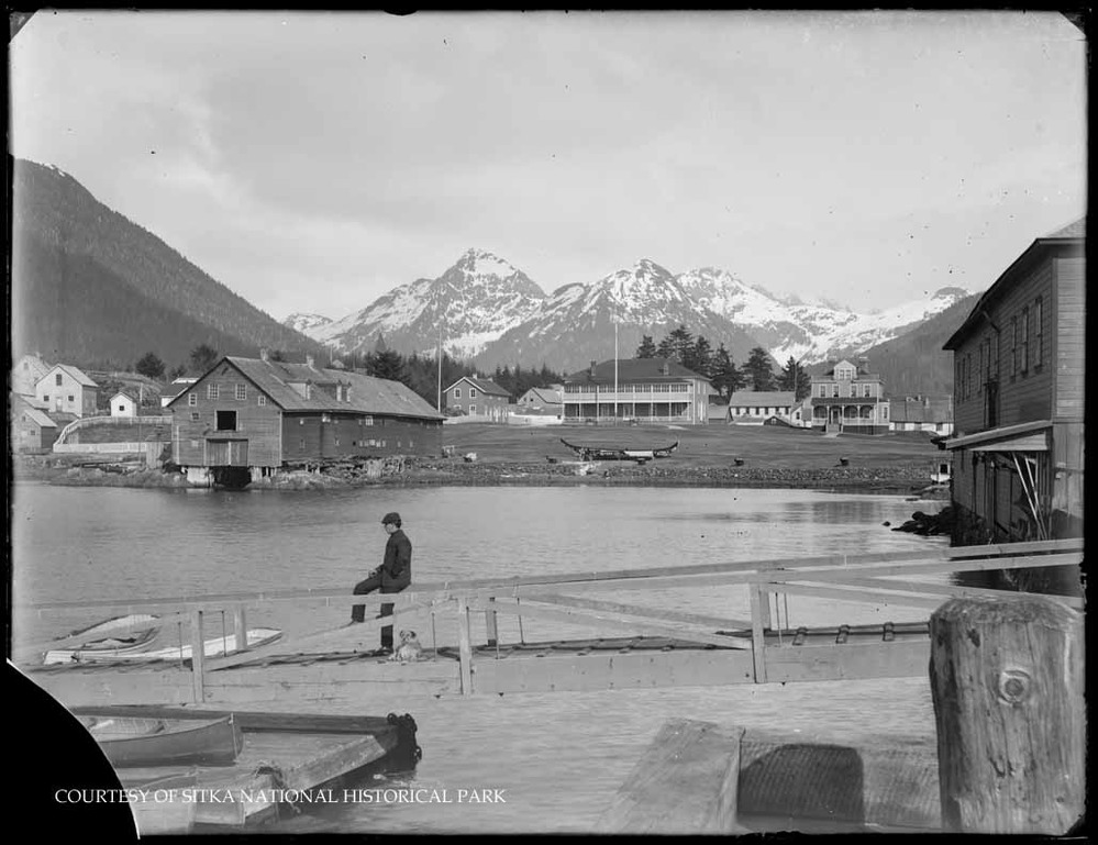 Parade grounds and surrounding Sitka Town with a man and his dog on a dock ramp in the foreground.