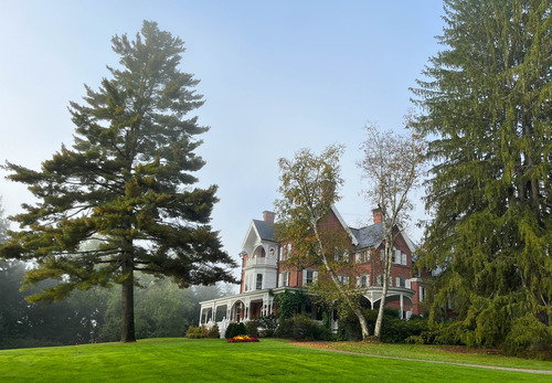 Red brick three-story mansion with white trim surrounded by landscaped garden and tall trees