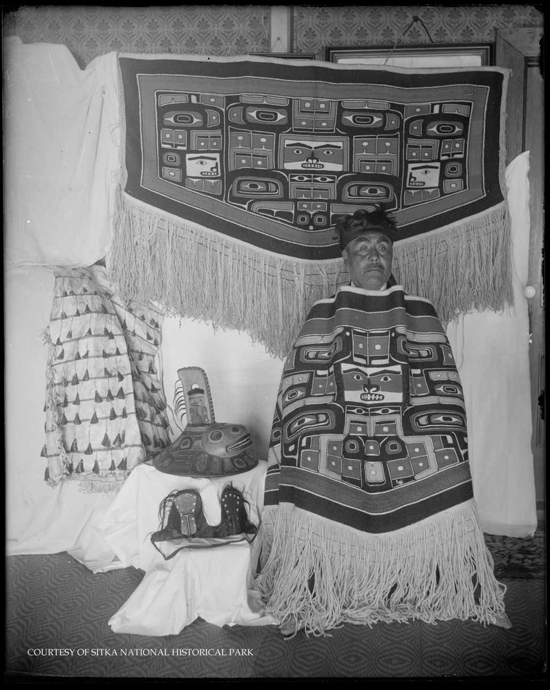 Man in ceremonial regalia with Chilkat robes; Killer Whale hat and other objects.