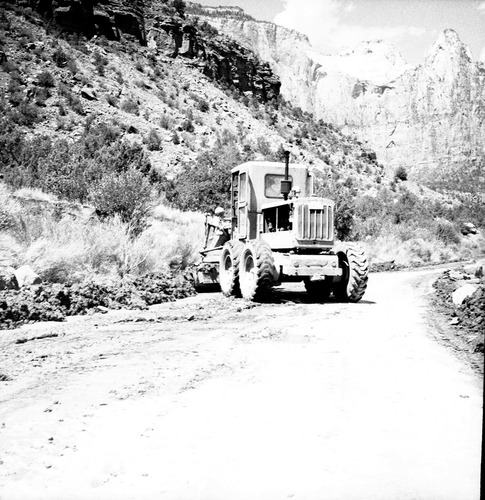 Grader clearing debris from roadway after flood damage.