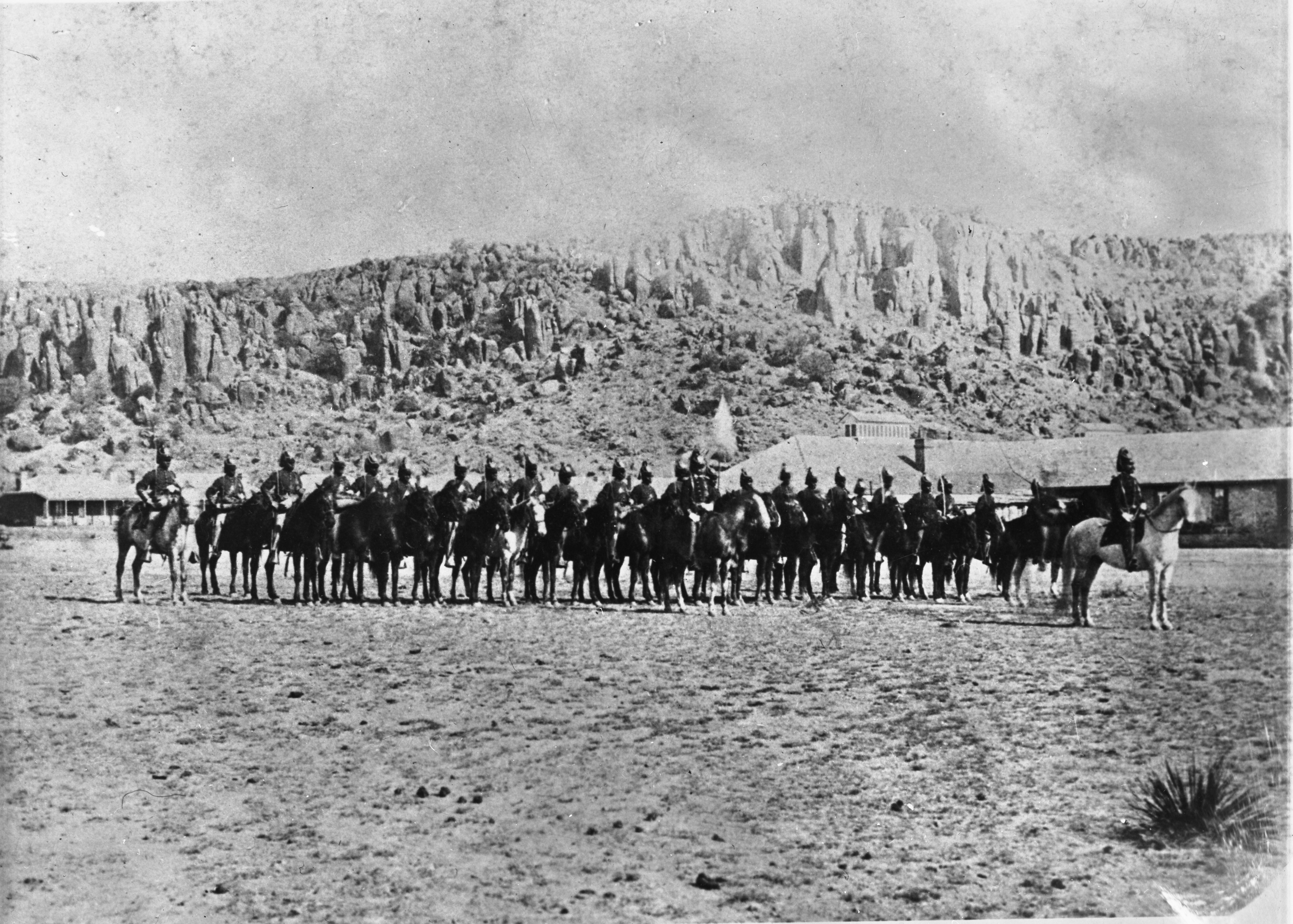 A historic image of soldiers on horseback in front of a desert landscape.