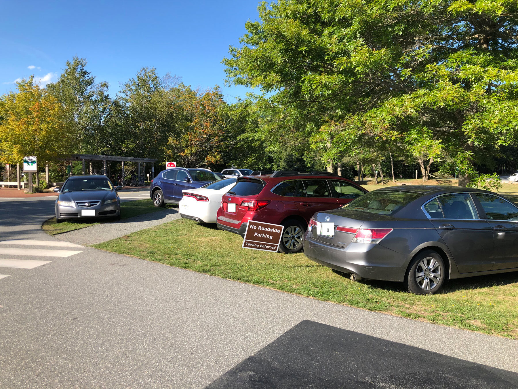 In front of a restaurant, cars park on the grass and over sidewalks in front of a 'no roadside parking' sign.